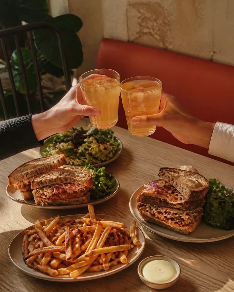 Deux personnes trinquent avec des limonades autour d’une table garnie de sandwichs et de frites.